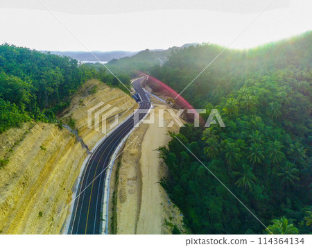 a curved road snaking through a dense green forest. 114364134