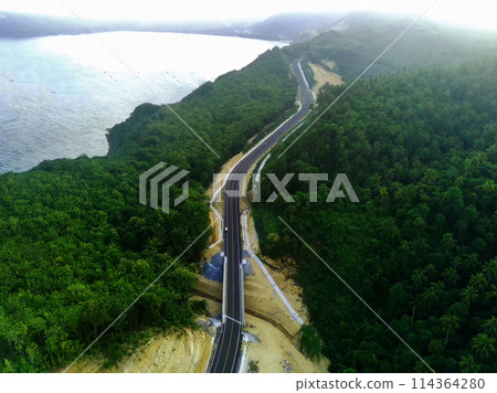 a curvy coastal road snaking along a bright blue ocean. 114364280