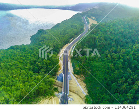 a curvy coastal road snaking along a bright blue ocean. 114364281