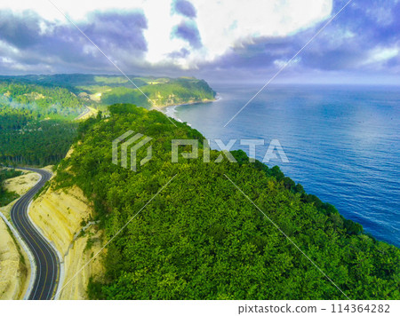 a curvy coastal road snaking along a bright blue ocean. 114364282