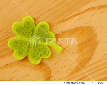 A green shamrock with four hearts on it is on a wooden surface 114364586
