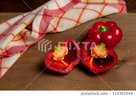 Whole and halves of red bell pepper on wooden background with red kitchen towel. . 114365049