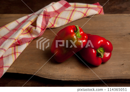 Two red bell pepper on wooden background with red kitchen towel. . 114365051
