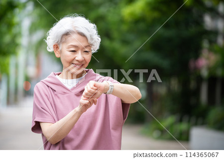 A gray-haired senior woman walking while wearing a smartwatch 114365067
