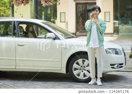 Young woman using a smartphone in front of a car 114365176