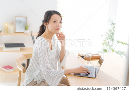 A woman in her 30s looking at a computer in her room A woman in her 30s looking at a computer in her room 114367427