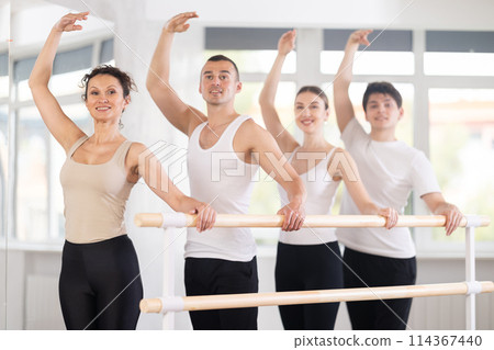 Woman practicing third position at barre at ballet group class Woman practicing third position at barre at ballet group class 114367440