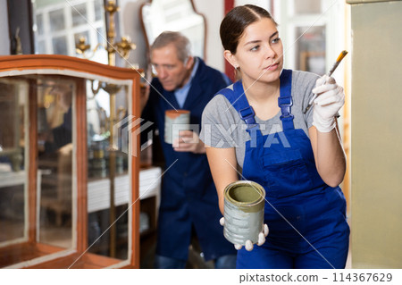 Young female furniture maker diligently working on vintage glass cabinet in workshop 114367629