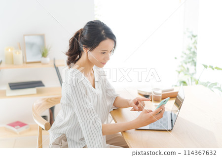 A woman in her 30s looking at a computer in her room A woman in her 30s looking at a computer in her room 114367632