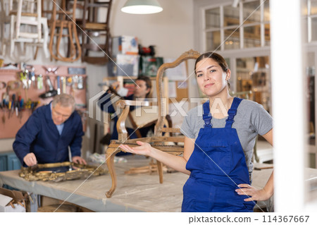 Smiling young female carpenter showing around local furniture workshop 114367667