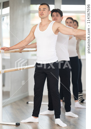 Man mastering second position at barre at group ballet class 114367696