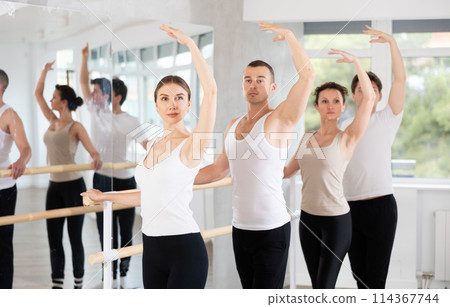 Group of positive young women and men engaged in classical ballet in dance studio performs exercise standing in 3rd position of ballet stance Group of positive young women and men engaged in classical ballet in dance studio performs exercise standing in 3rd position of ballet stance 114367744