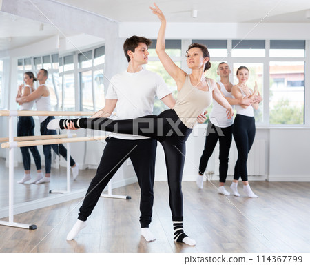 Happy young caucasian man and woman practicing ballet arabesque pose in ballroom Happy young caucasian man and woman practicing ballet arabesque pose in ballroom 114367799