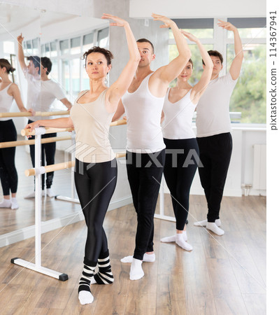 Group of dancers stand in fifth position at barre 114367941