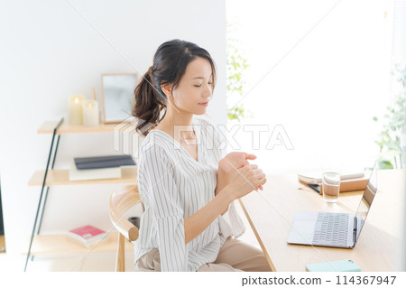 A woman in her 30s looking at a computer in her room A woman in her 30s looking at a computer in her room 114367947