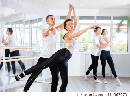 Young active man engaged in dance hall with female partner and practicing ballet arabesque pose during group class. Hobby lifestyle concept Young active man engaged in dance hall with female partner and practicing ballet arabesque pose during group class. Hobby lifestyle concept 114367973