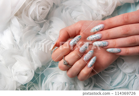 Female hands with blue nail design on blue silk background. 114369726