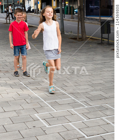 Funny children play hopscotch on the sidewalk in the city 114369808