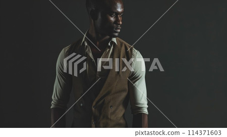 Stylish African American Man in Casual Attire Posing in Dark Studio 114371603