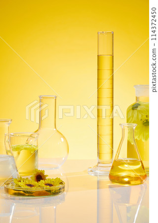 Frontal photo with plenty items of laboratory and calendula placed on white flat form over yellow background. Calendula has been used to treat a variety of skin conditions Frontal photo with plenty items of laboratory and calendula placed on white flat form over yellow background. Calendula has been used to treat a variety of skin conditions 114372450