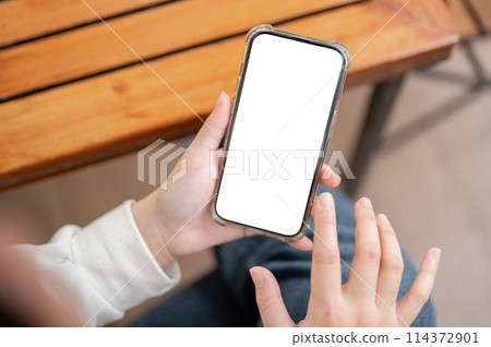 A close-up image of a woman in casual clothes using her smartphone at a table indoors. 114372901