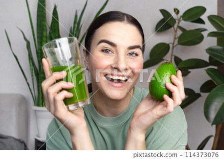 Woman is happy, she smiling and shows green wheatgrass drink and avocado. Healthy lifestyle concept, green healthy vegetables and fruits. Woman is happy, she smiling and shows green wheatgrass drink and avocado. Healthy lifestyle concept, green healthy vegetables and fruits. 114373076
