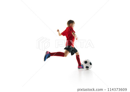 Sporty little boy, kicks ball to make perfect pass in motion against white studio background. Small football player makes goal 114373609