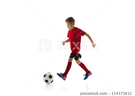 Little athlete boy, dribbling ball to take perfect goal against white studio background. Young soccer player in motion. 114373612