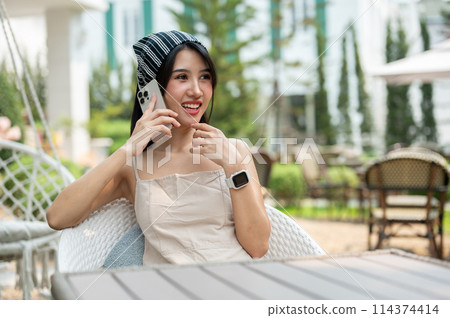 A beautiful Asian woman sits in a beautiful English garden talking on the phone with her friend. A beautiful Asian woman sits in a beautiful English garden talking on the phone with her friend. 114374414