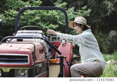 A tractor and a woman standing in front of a field 114375691