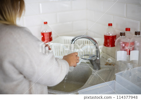 A woman standing with her back is washing a plastic bottle in the sink A woman sorts plastic in the kitchen of her home for recycling. Concept of eco-friendly lifestyle plastic recycling world trend. 114377948