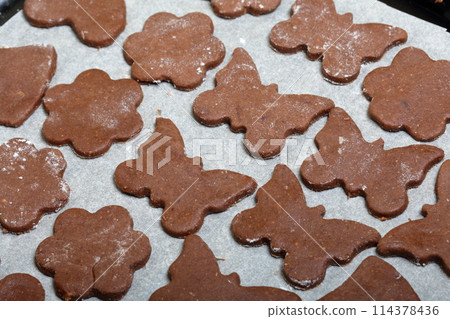 On the baking sheet laid blanks for baking gingerbread. They are on food paper. Cooking gingerbread. On the baking sheet laid blanks for baking gingerbread. They are on food paper. Cooking gingerbread. 114378436