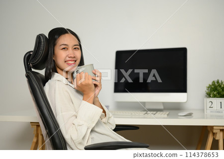 Attractive young businesswoman drinking coffee at the desk in the office 114378653
