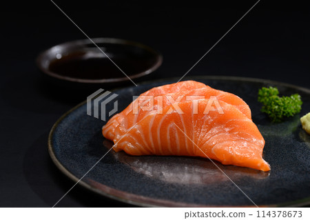 Close up sliced salmon sashimi serve on black plate with parsley leaf. Japanese food style Close up sliced salmon sashimi serve on black plate with parsley leaf. Japanese food style 114378673