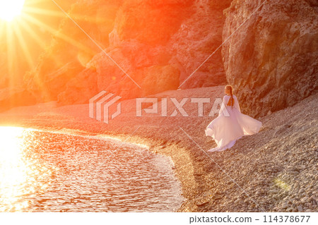 Mysterious woman silhouette long hair walks on the beach ocean water, sea nymph wind listens to the wave. Throws up a long white dress, a divine sunset. Artistic photo from the back without a face Mysterious woman silhouette long hair walks on the beach ocean water, sea nymph wind listens to the wave. Throws up a long white dress, a divine sunset. Artistic photo from the back without a face 114378677