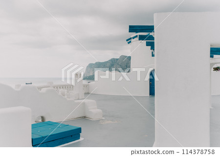 A blue and white building with a blue door sits on a balcony overlooking the ocean. The scene is serene and peaceful. A blue and white building with a blue door sits on a balcony overlooking the ocean. The scene is serene and peaceful. 114378758