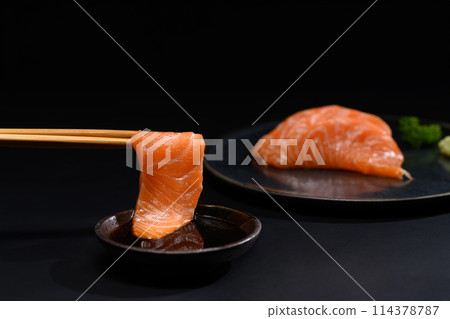 Closeup chopsticks with fresh salmon sashimi dipping into soy sauce. Japanese food style 114378787