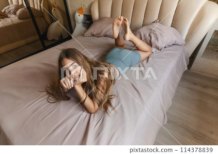 A girl is laying on a bed with her head on her hand. She is looking up at the ceiling. 114378839
