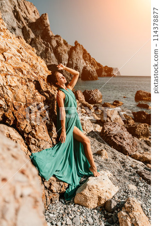 Woman green dress sea. Woman in a long mint dress posing on a beach with rocks on sunny day. Girl on the nature on blue sky background. Woman green dress sea. Woman in a long mint dress posing on a beach with rocks on sunny day. Girl on the nature on blue sky background. 114378877
