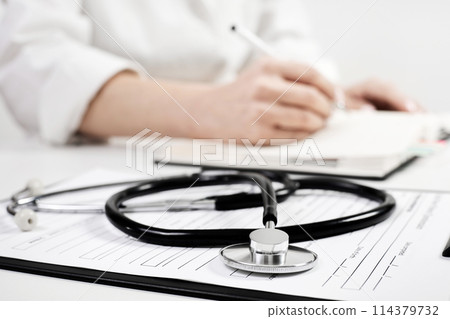 Phonendoscope on the background of a doctor who writes something in a notebook 114379732