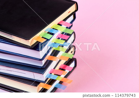 Close-up of a stack of office notepads with colorful sticky page markers sandwiched between pages on pink background Close-up of a stack of office notepads with colorful sticky page markers sandwiched between pages on pink background 114379743