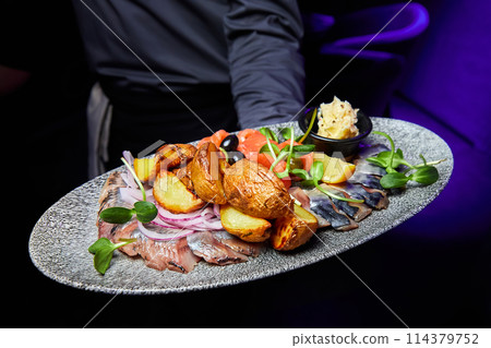 The waiter holds a plate with Atlantic Fish Plate with Onions, Baked Potato Pieces and Cream Sauce The waiter holds a plate with Atlantic Fish Plate with Onions, Baked Potato Pieces and Cream Sauce 114379752