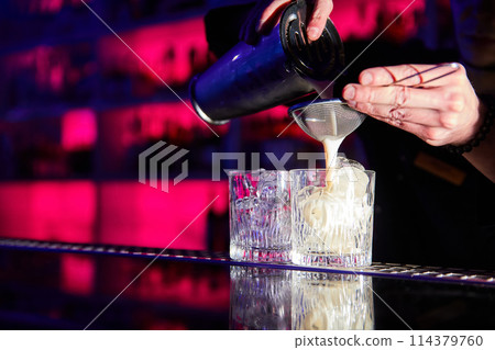 The bartender prepares cocktails on the bar counter using a shaker and a strainer 114379760