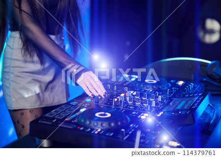 Dj girl playing music with turntables and sound mixer on stage in night club 114379761
