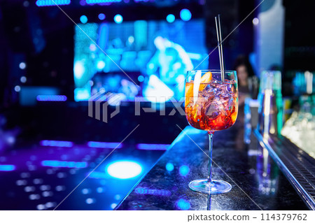 Alcoholic cocktail with ice and a piece of orange on the bar counter 114379762