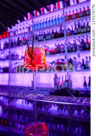 Alcoholic cocktail with ice and a piece of orange on the bar counter Alcoholic cocktail with ice and a piece of orange on the bar counter 114379776