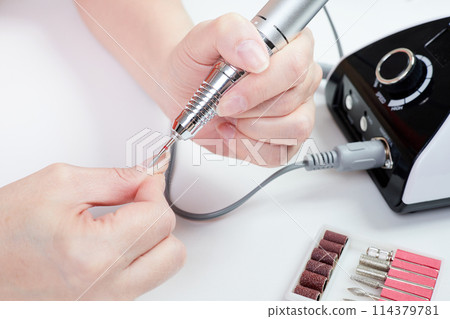 A girl gives herself a manicure using a nail drill 114379781