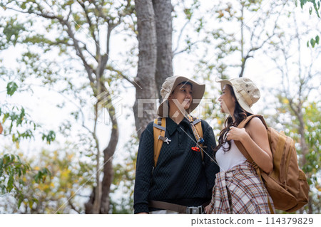Cheerful romantic lesbian couple traveler with backpack on their backs go hiking through the forest in the mountains in summer 114379829