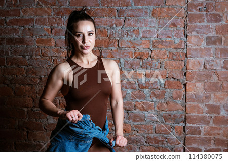 A woman in brown tank top is standing in front of a brick wall 114380075