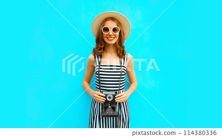 Summer portrait happy smiling young woman photographer with camera in straw hat on blue background 114380336